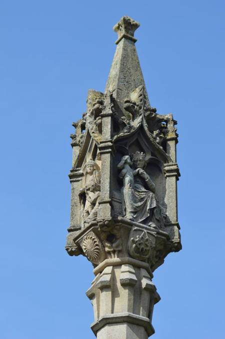The carved head of the memorial cross against a blue sky, showing a figure in a canopied niche.