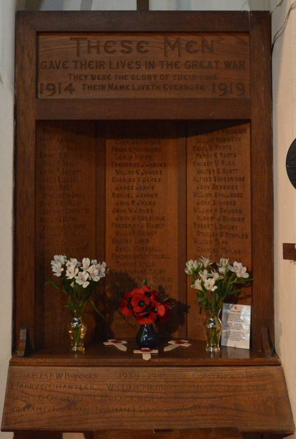 The carved oak war memorial in Holy Trinity Church, Larkfield, with poppies and white flowers on the ledge below the names.