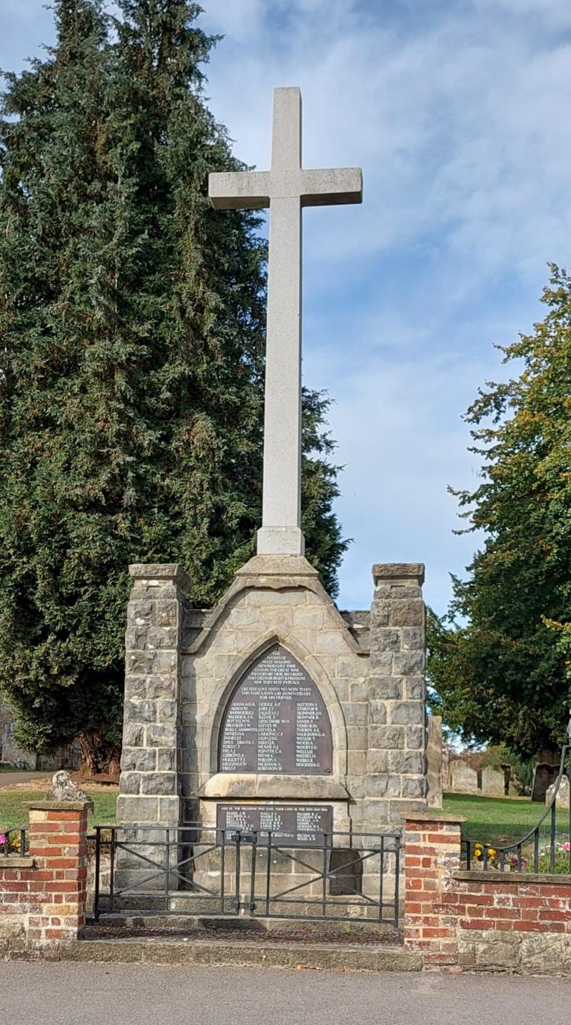 The West Malling war memorial: a tall stone cross above a ragstone screen with the two name plaques, behind railings at the edge of St Mary's churchyard.